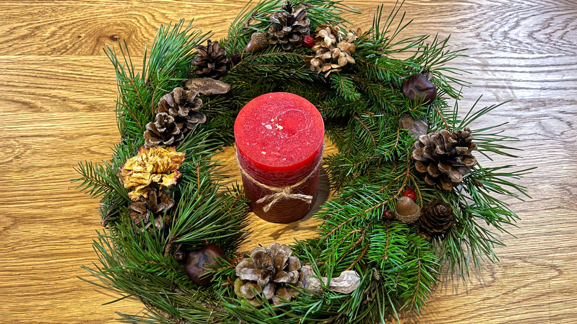 selbstgebundener Adventskranz aus Tannengrün und Zapfen mit roter Kerze in der Mitte